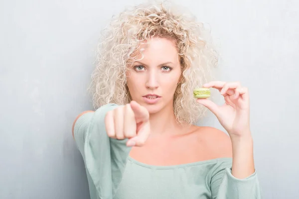 Joven Rubia Sobre Fondo Gris Grunge Comiendo Macaron Señalando Con —  Fotos de Stock