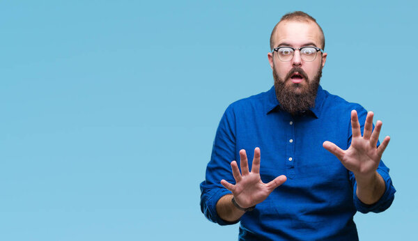 Young caucasian hipster man wearing glasses over isolated background afraid and terrified with fear expression stop gesture with hands, shouting in shock. Panic concept.
