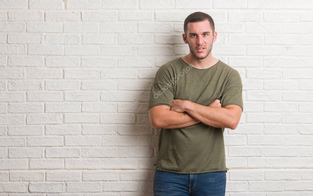 Young caucasian man standing over white brick wall skeptic and nervous, disapproving expression on face with crossed arms. Negative person.