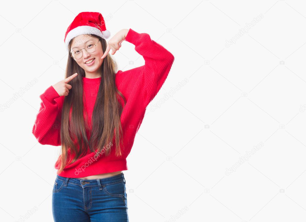 Young Chinese woman over isolated background wearing christmas hat smiling confident showing and pointing with fingers teeth and mouth. Health concept.