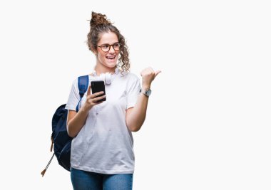 Sırt çantası, kulaklık ve akıllı telefon işaret ve başparmak kadar mutlu yüz gülümseyen tarafı ile gösteren izole arka plan üzerinde giyen genç esmer öğrenci kız