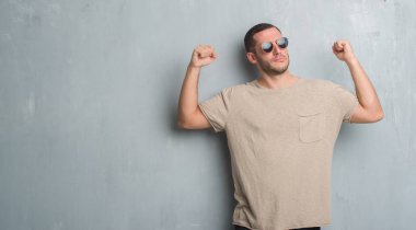 Beyaz delikanlı gösterilen kol kasları gururlu gülümseyen güneş gözlüğü takıyor gri grunge duvarın üzerinden. Fitness kavramı.