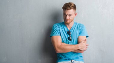 Gri grunge duvar yüz çapraz silah ile rahat kıyafet şüpheci ve sinir, onaylamayan ifade giyen genç Kızıl saçlı adam. Negatif kişi.