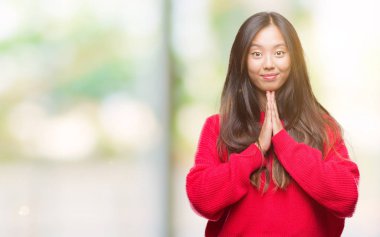 Ellerle birlikte AF emin gülümseyen için soran dua izole arka plan üzerinde kış kazak giyen genç Asyalı kadın.