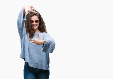 Güzel esmer kıvırcık saçlı Genç kız elle yapma çerçeve ve parmakları ile mutlu yüz gülümseyen izole arka plan üzerinde güneş gözlüğü takıyor. Yaratıcılık ve Fotoğrafçılık kavramı.