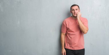 Beyaz delikanlı stresli ve gergin elle çivi ısırma ağzına seyir gri grunge duvarın üzerinden. Anksiyete sorunu.