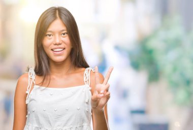 Genç Asyalı kadın mutlu yüz zafer işareti yaparken kameraya göz kırpıyor ile gülümseyen izole arka plan üzerinde. İki numaralı.