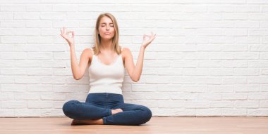 Güzel genç kadın oturan kat evde dinlenmek ve gülümseyen gözlerle parmak ile meditasyon jest yapıyor kapalı. Yoga kavramı.