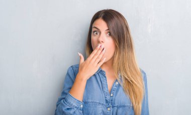 Hata, korku, sessizlik içinde gizli kavramı korkmuş ifade için utanç ile gri grunge duvar denim kıyafet kapak ağız el ile giyen genç yetişkin kadın şok