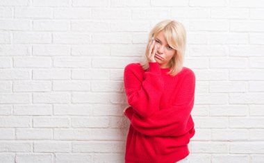 Beyaz tuğla duvar kış kazak düşünme seyir giyiyor yetişkin beyaz kadın yorgun ve sıkılmış çapraz silah depresyon sorunları ile.