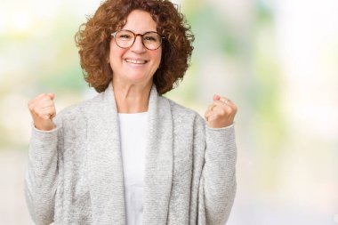 Ceket ve gözlük izole arka plan kutlama üzerinde giyen güzel orta ager üst düzey kadın şaşırttı ve başarı için kaldırdı kollarını açarak hayret ve gözleri açık. Kazanan kavramı.