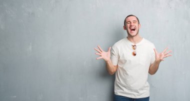 Beyaz delikanlı deli ve deli bağırarak ve agresif ifade ve silah kaldırdı bağırmaya güneş gözlüğü takıyor gri grunge duvarın üzerinden. Hayal kırıklığı kavramı.