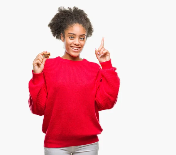 Young Afro American Woman Eating Chocolate Macaron Isolated Background Surprised — Stock Photo, Image