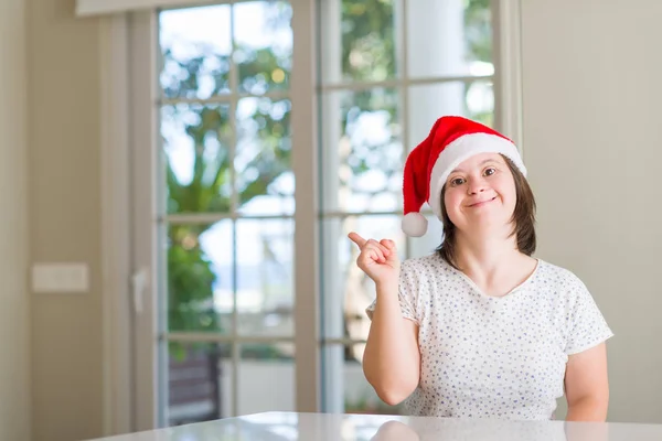 唐氏综合症妇女在家里戴着圣诞帽非常高兴用手和手指指着旁边 — 图库照片
