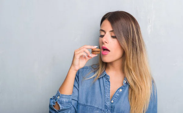 Young Adult Woman Grey Grunge Wall Eating Chocolate Macarons Confident — Stock Photo, Image