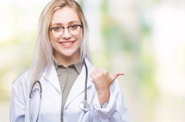年轻的金发医生的女人在孤立的背景微笑着快乐的脸 并指向侧面与拇指向上 — 图库照片