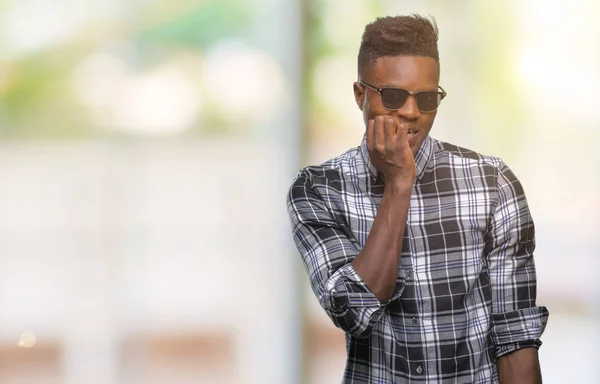 年轻的非洲裔美国男子戴着太阳镜在孤立的背景下看着压力和紧张的嘴咬指甲的手 焦虑问题 — 图库照片