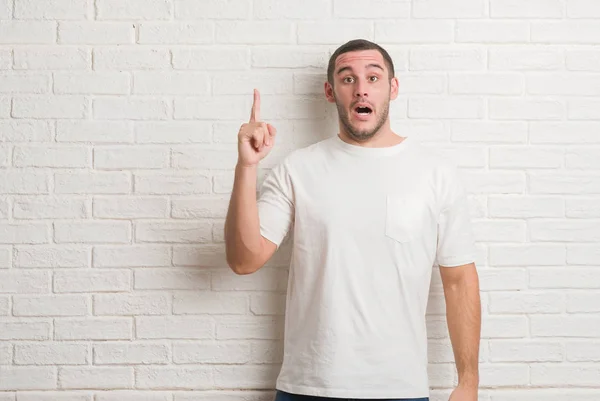 Kaukasische Jongeman Permanent Witte Bakstenen Muur Wijzende Vinger Omhoog Met — Stockfoto