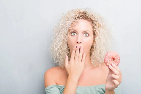 間違い 沈黙の中 秘密の概念で怖いの表現のための恥とショックを受けた手でピンク ドーナツ カバー口を食べるグランジ灰色の背景の上の若いブロンドの女性 — ストック写真