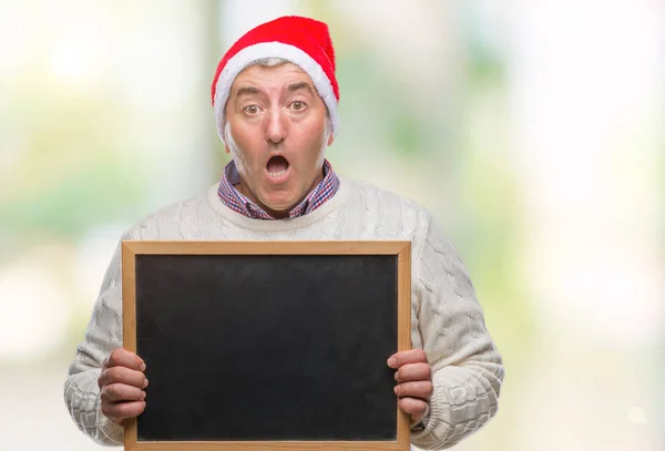 英俊的老人戴着圣诞帽 拿着黑板在孤立的背景上 惊讶地吓得目瞪口呆 害怕和兴奋的恐惧表情 — 图库照片