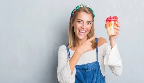 非常に幸せな手と指で指している果物を食べるグランジ灰色の壁に美しい若い女性 — ストック写真