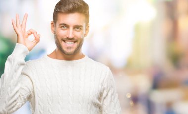 İzole arka plan el ve parmaklar ok işaretiyle yapıyor olumlu gülümseyen üzerinde kış kazak giyen genç yakışıklı adam. Başarılı ifade.