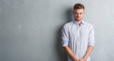 Komik surat ile yanakları şişirme gri grunge duvarın üzerinden genç redhead iş adamı. Ağız ile hava, deli ifade şişirilmiş.