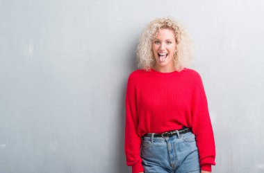 Dilini grunge gri arka plan üzerinde Kıvırcık saçlı sarışın genç kadın out komik ifade ile mutlu. Duygu kavramı.