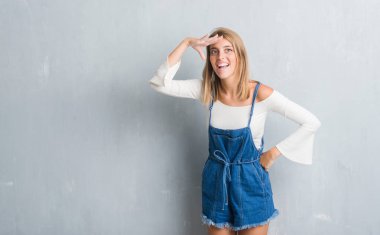 Grunge gri duvardan çok mutlu ve gülümseyen uzakta el ile üzerine kafa seyir duran güzel genç kadın. Arama kavramı.