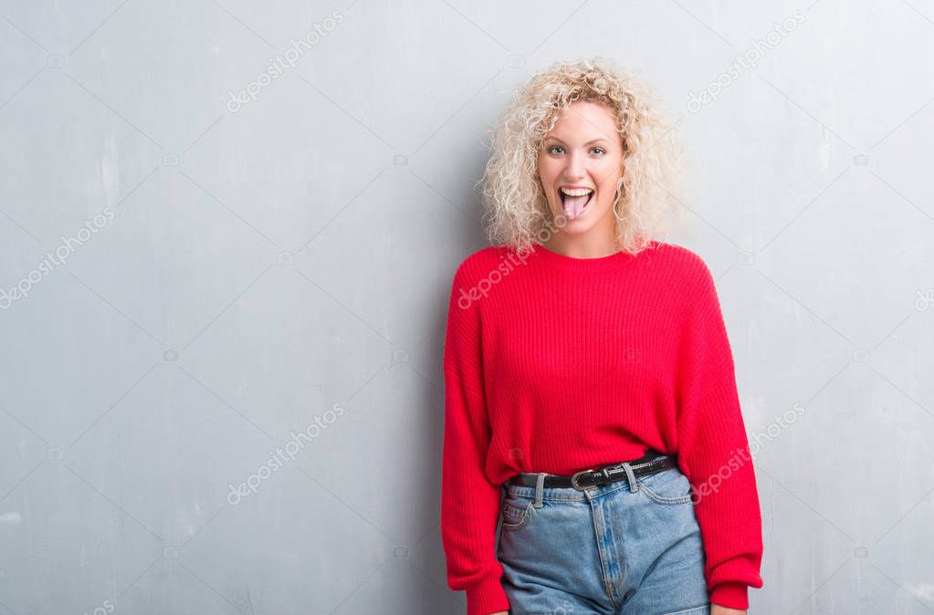 Young blonde woman with curly hair over grunge grey background sticking tongue out happy with funny expression. Emotion concept.