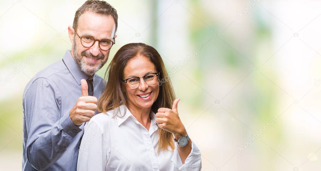 Middle age hispanic couple in love wearing glasses over isolated background doing happy thumbs up gesture with hand. Approving expression looking at the camera with showing success.