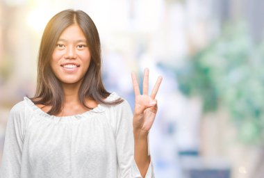 Genç Asyalı kadın gösterilen ve parmakları ile işaret izole arka plan üzerinde üçüncü ise kendinden emin ve mutlu gülümseyerek.