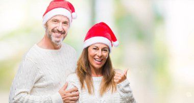 Orta yaş İspanyol çift arıyorum ve başparmak yanında yukarıyı mutlu yüz ile gülümseyen izole arka plan üzerinde Noel şapka.