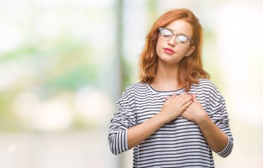 İzole arka plan ile gülümseyen gözlüklü genç güzel kadın kapalı gözler ve yüzünde minnettar jest ile göğüs üzerinde eller. Sağlık kavramı.