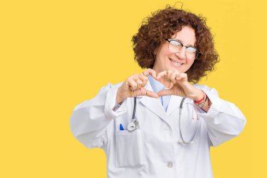 Orta ager kıdemli doktor kadın kalp simgesi ve elleriyle şekil gösterilen aşık gülümseyen izole arka plan yüzünden. Romantik kavramı.