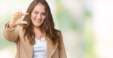 Güzel izole arka plan üzerinde kış ceket giyen boyutu genç kadın artı gülümseyen ve boyutu işi el ile kendinden emin eller parmakları ile seyir ve fotoğraf makinesi oturum açın. Ölçü kavramı.