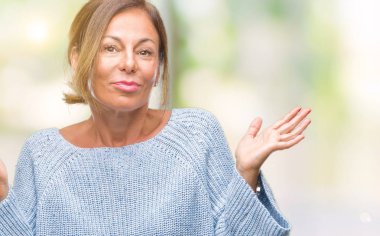 Üzerinde kış kazak giyen orta yaş üst düzey İspanyol kadın arka plan clueless ve şaşkın bir ifadeyle kollar ve eller kaldırdı izole. Şüphe kavramı.