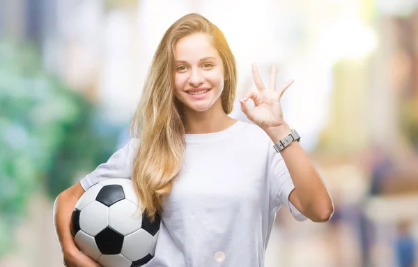 年轻美丽的金发碧眼的女人拿着足球在孤立的背景做确定的标志与手指 优秀的象征 — 图库照片