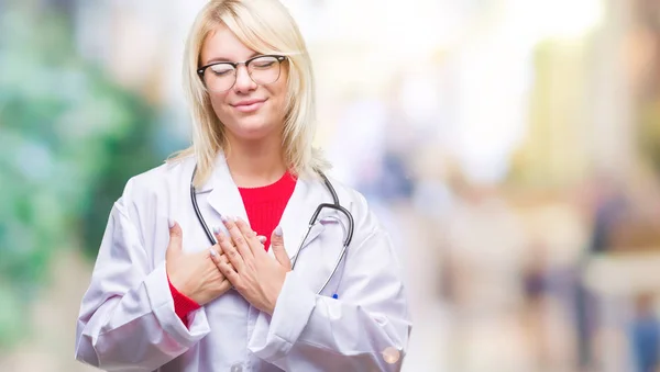 目を閉じて胸に手と感謝のジェスチャーの顔に笑みを浮かべて隔離された背景に医療制服を着て美しい金髪女医女性 健康の概念 — ストック写真