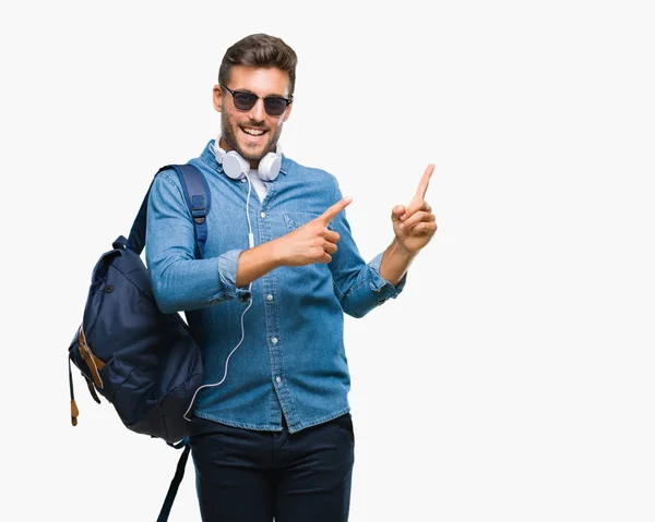 若いハンサムな観光客男分離背景笑顔で側に つの手と指で指しているカメラ目線の上身に着けているヘッドフォンとバックパック — ストック写真
