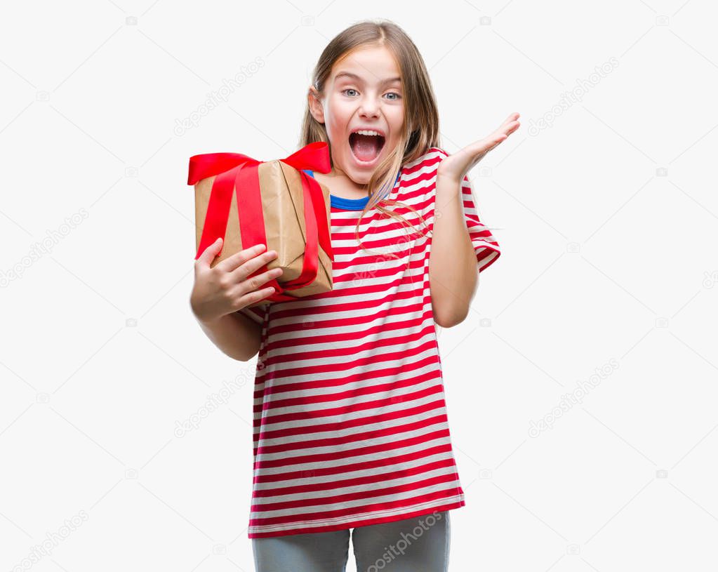 Young beautiful girl giving christmas or valentine gift over isolated background very happy and excited, winner expression celebrating victory screaming with big smile and raised hands