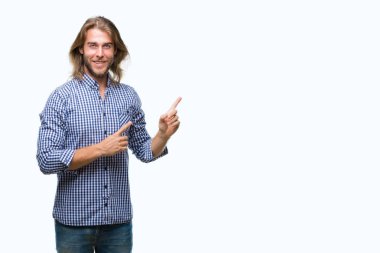 Gülümseyen ve iki elleri ve parmakları ile tarafına işaret kamera bakarak izole arka plan üzerinde uzun saçlı yakışıklı delikanlı.