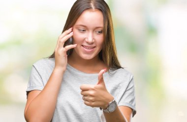 Genç güzel beyaz kadın söz Smartphone'da mutlu izole arka plan üzerinde ok işareti, başparmak ile parmak, mükemmel işareti yapıyor kocaman bir gülümseme ile