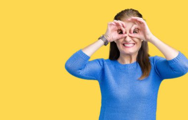 Dilini, parmaklarının arasından baktığını yapışmasını dürbün gibi ok jest yapıyor izole arka plan üzerinde kış kazak giyen güzel orta yaş Olgun kadın. Deli ifade.