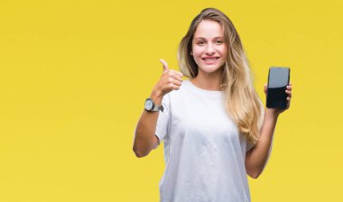 Güzel, sarışın bir kadın, izole edilmiş arka planda akıllı telefon ekranı gösteriyor. Kocaman gülümsüyor ve gülümsüyor. İşaret veriyor.