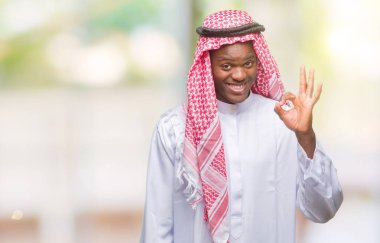 Geleneksel keffiyeh izole arka plan el ve parmaklar ok işaretiyle yapıyor olumlu gülümseyen üzerinde giyen genç Arapça Afrika adam. Başarılı ifade.