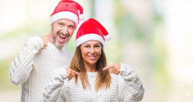 Orta yaş İspanyol çift izole arka plan ile kendine güvenen seyir üzerinde Noel şapka kendini gururlu ve mutlu parmakları ile işaret yüzündeki gülümseme.