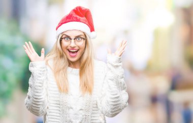 Üzerinde Noel şapka giyen genç güzel sarışın kadın deli kutluyor arka plan izole ve başarı için kaldırdı kollarını açarak hayrete ve heyecanlı çığlık gözleri açık. Kazanan kavramı