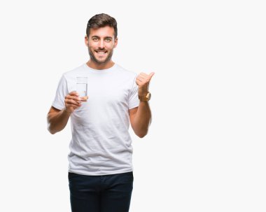 Yakışıklı delikanlı işaret ve başparmak kadar mutlu yüz gülümseyen tarafı ile gösteren izole arka plan üzerinde bardak su içme