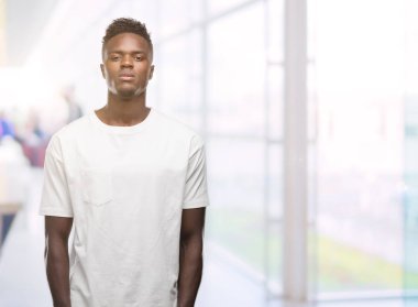 Yüzünde ciddi bir ifade ile beyaz t-shirt giyen genç Afro-Amerikan adam. Basit ve doğal kameraya bakıyor.